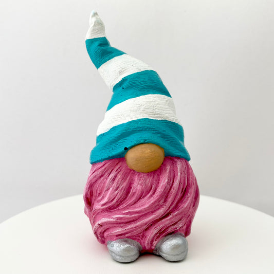 A small hand painted gonk statue with a teal and white striped hat, pink beard and silver shoes. 