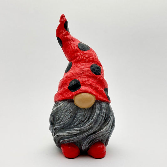 A small hand painted gonk statue with a Red and Black Spotty Ladybug Hat, a grey beard and red shoes. Front view.
