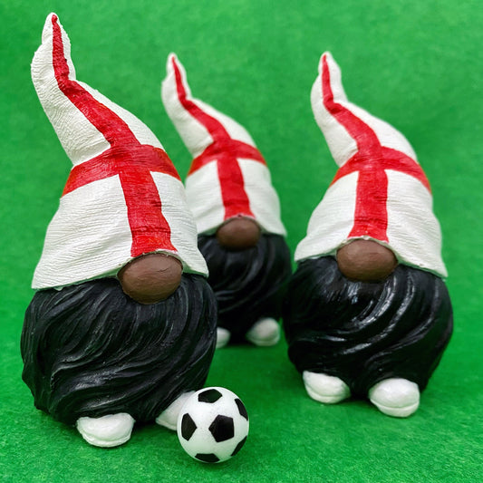 3 small hand painted gonk statues with an England Flag hat, black beard and white shoes. There is a mini football infront of them. The background is green.