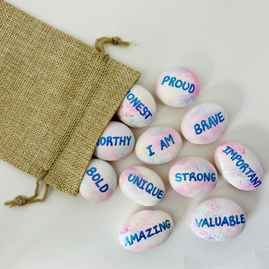A hessian bag with hand painted affirmation pebbles spilling out