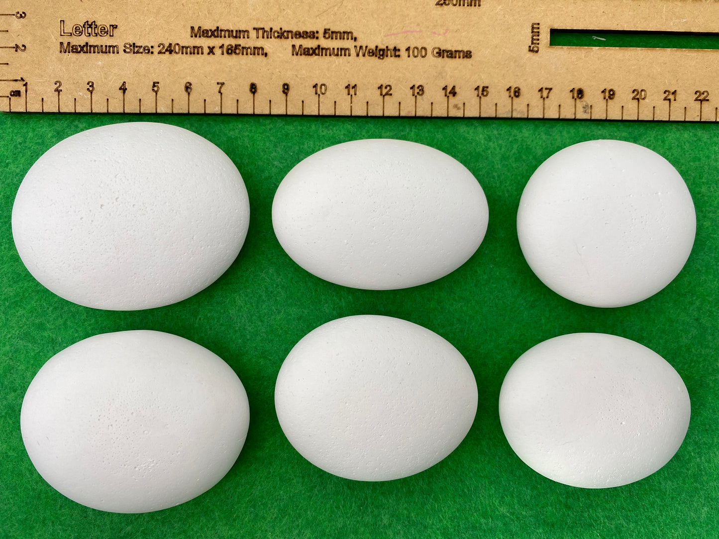 6 large white plaster pebbles of different shapes and sizes next to a ruler