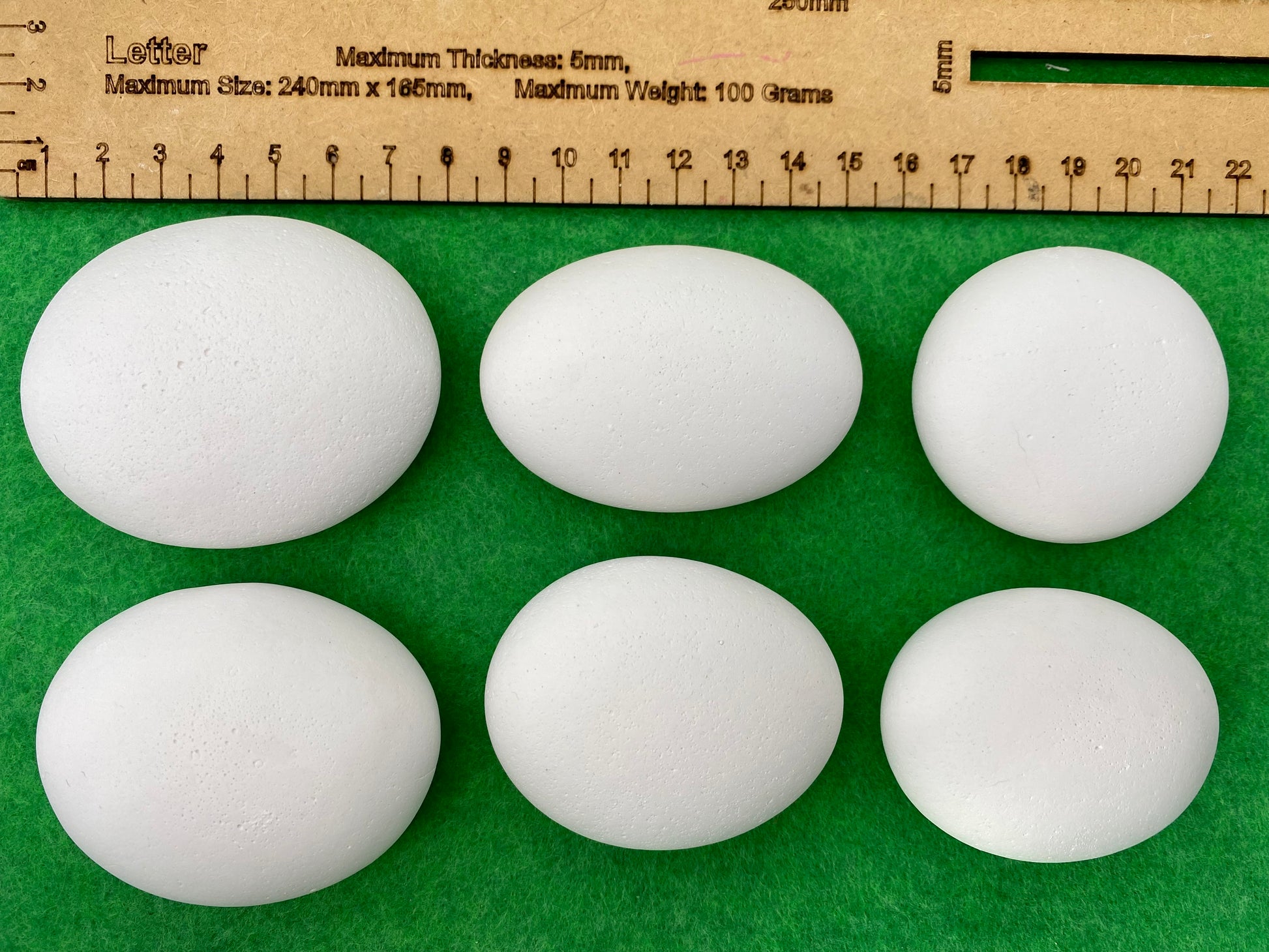 6 large white plaster pebbles of different shapes and sizes next to a ruler