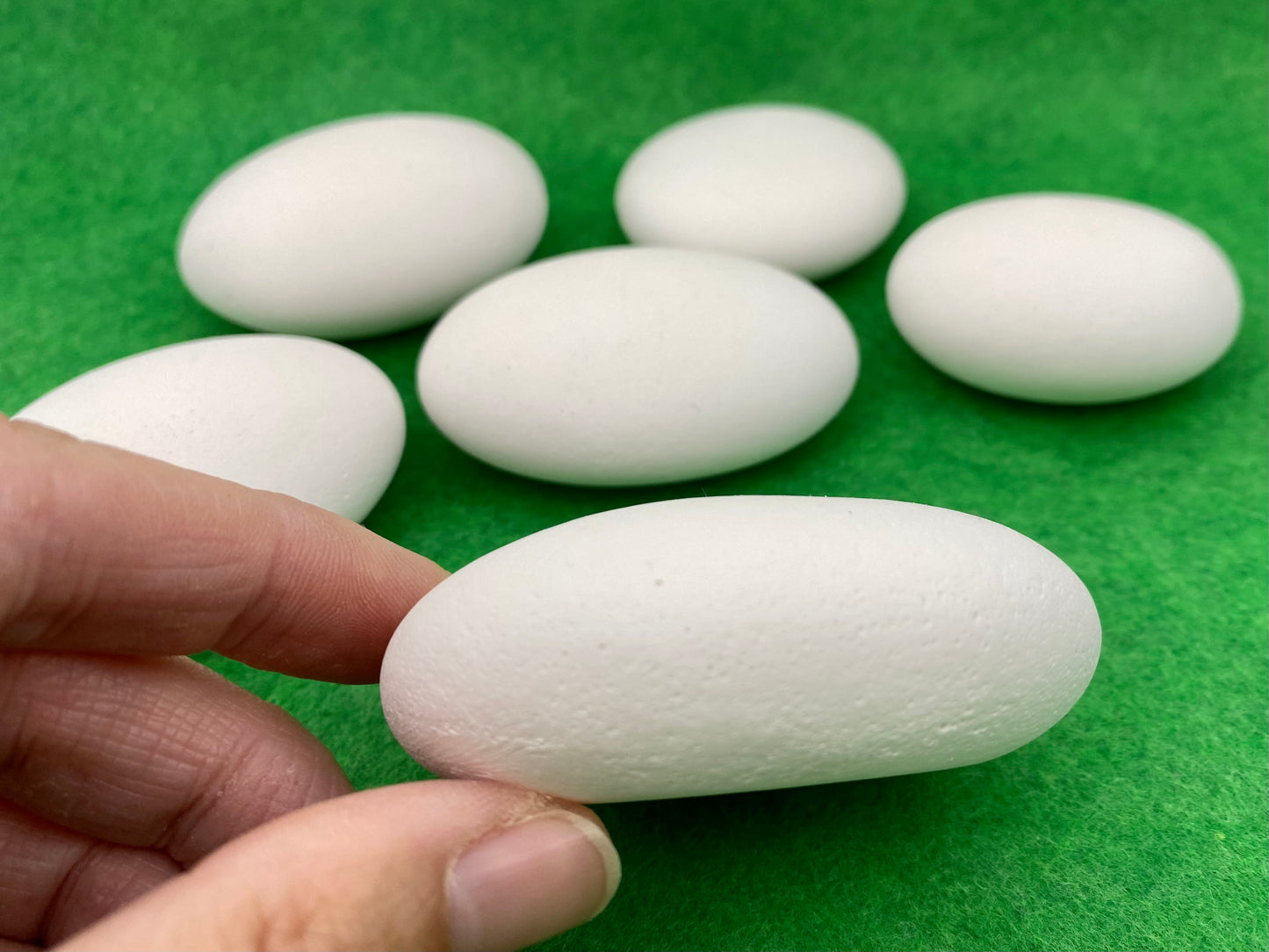 Side view of a Large white plaster pebble being held