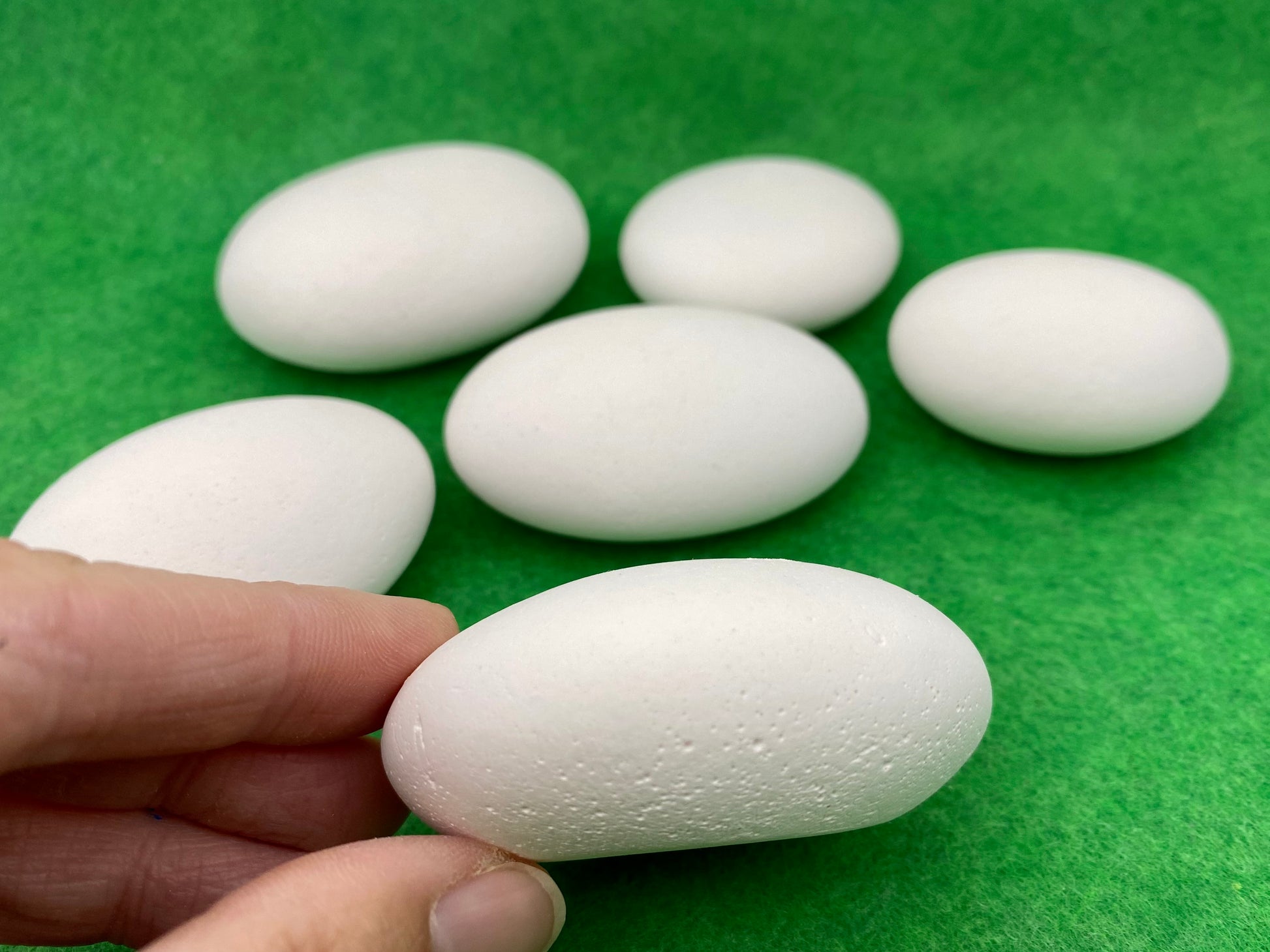 Side view of a Large white plaster pebble being held