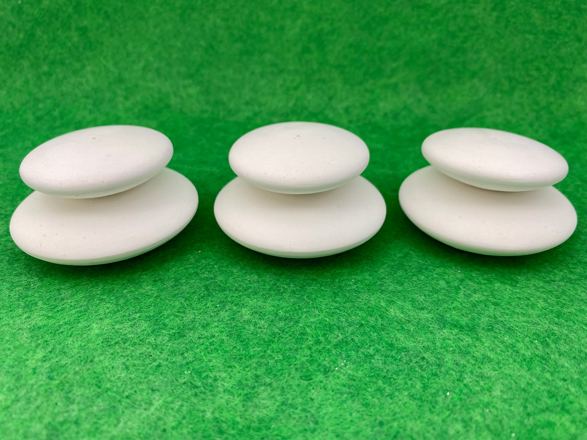 6 small white circular plaster pebbles in 2 sizes, stacked on top of each other