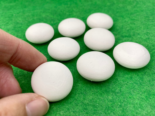 8 tiny white circular plaster pebbles, one being held by a hand