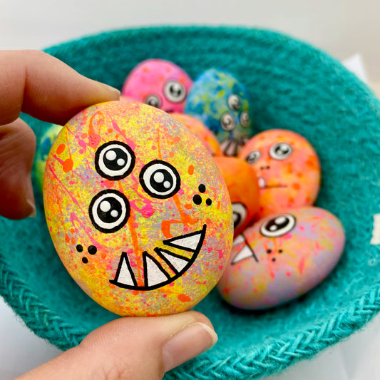 A hand painted 3 eyed monster pebble called Plarp being held by a hand