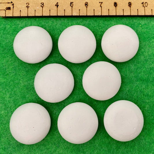 8 tiny white circular plaster pebbles next to a ruler