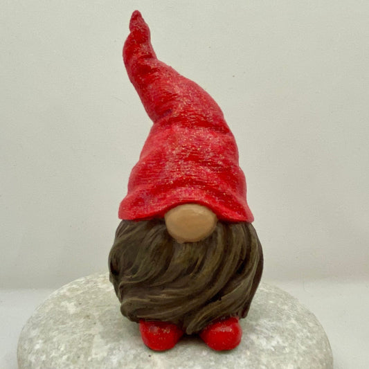 A small hand painted gonk statue with a red sparkly Hat, a brown Beard and red Shoes. Front view.