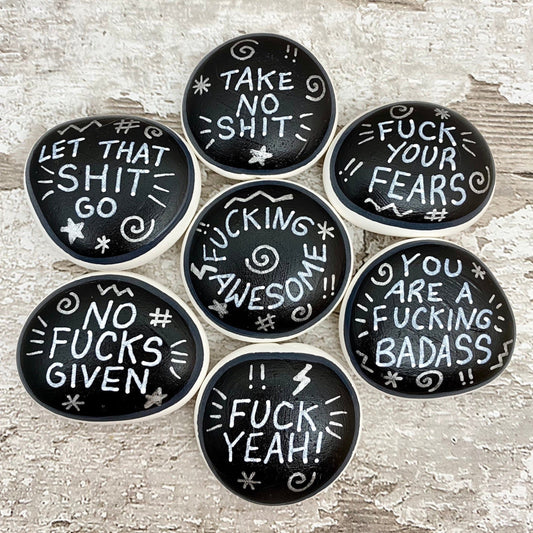 Hand painted Sweary Pebbles with rude affirmation messages. Silver words on a black background