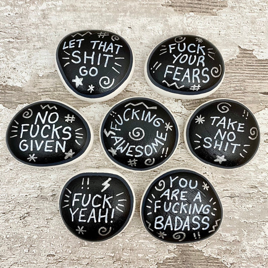 Hand painted Sweary Pebbles with rude affirmation messages. Silver words on a black background