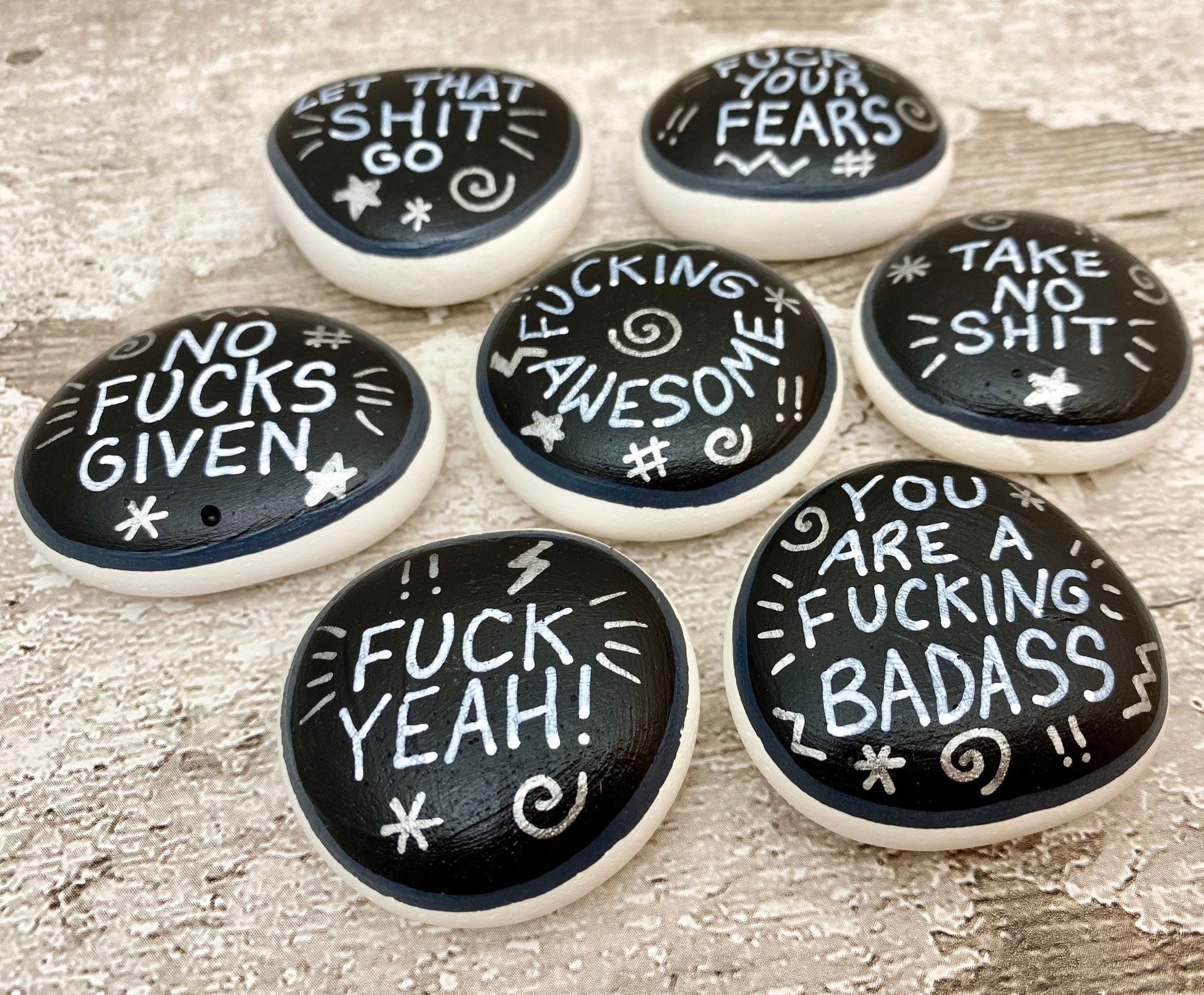 Hand painted Sweary Pebbles with rude affirmation messages. Silver words on a black background
