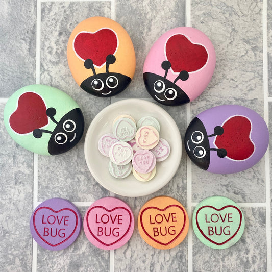 4 Hand painted Pastel Heart Bug Pebbles and Tokens with the words Love Bug inscribed on and a plate of Love Hearts